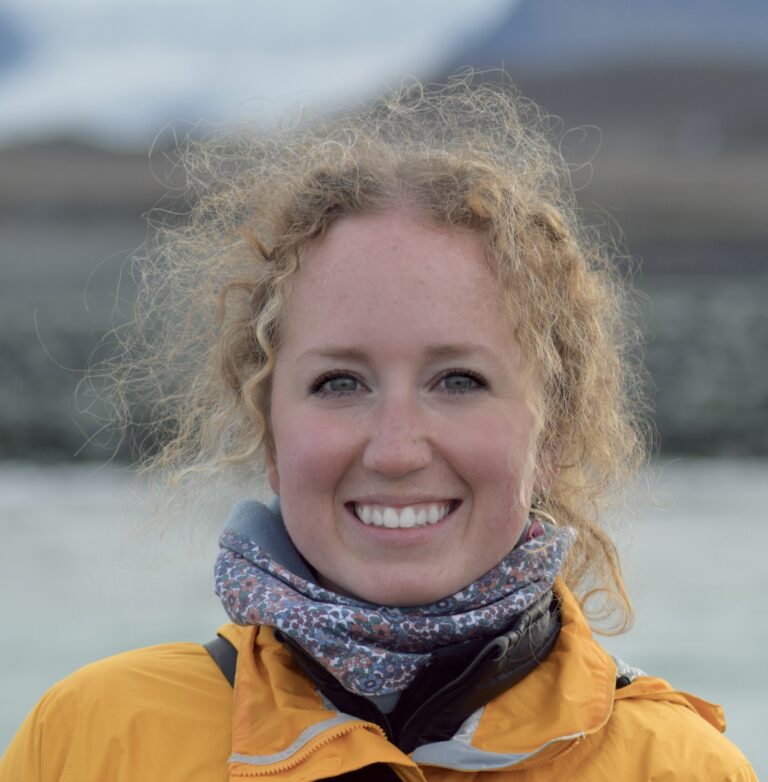 person with blond hair and yellow coat outside with water in background