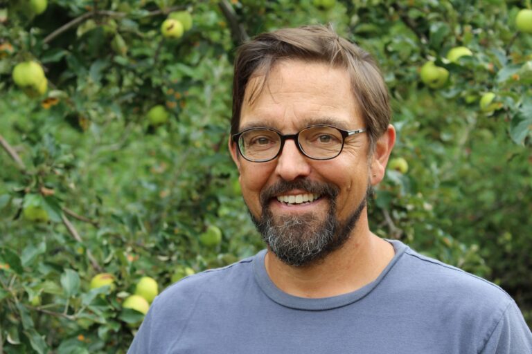 todd outside, smiling in front of apple trees