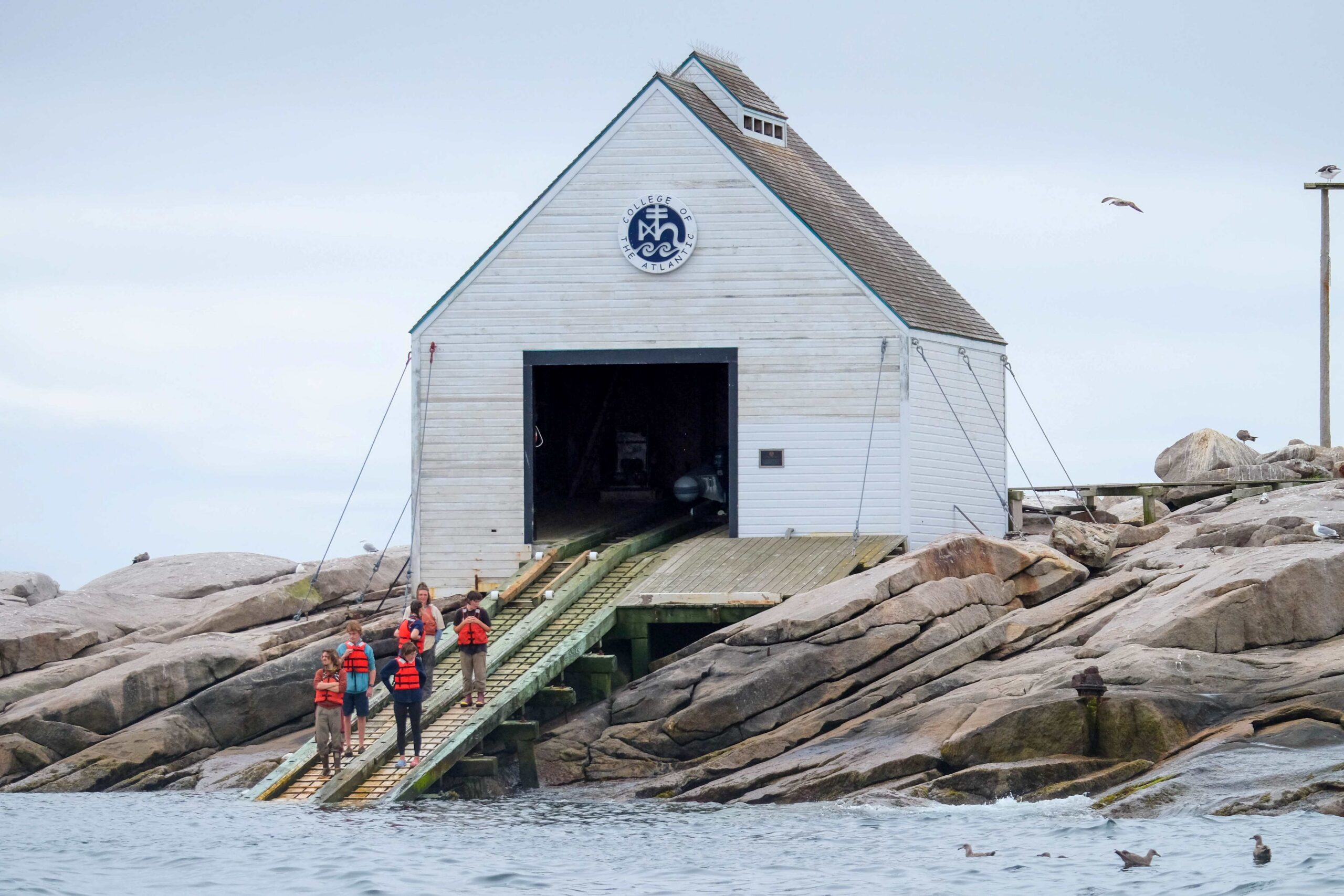 students on boat ramp with boat shed behind